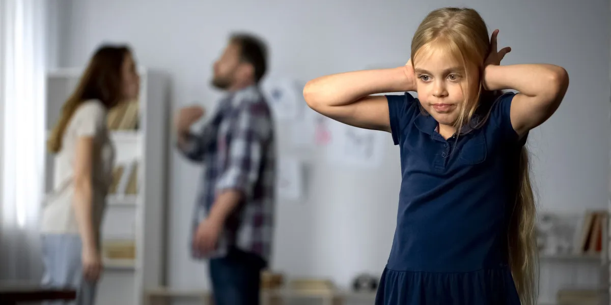Small child blocking ears with parents arguing in background