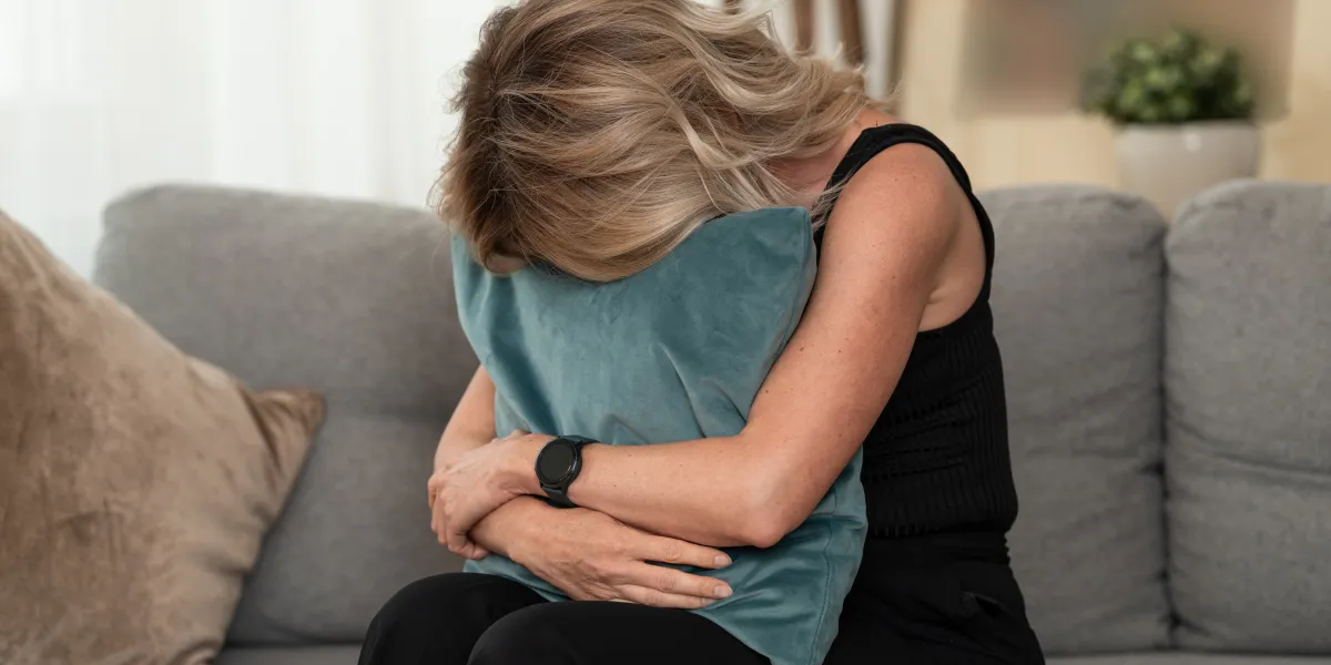 Woman crying into her pillow while sitting alone on her couch