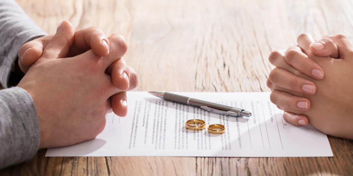partners signing a divorce paper with their wedding rings on the table